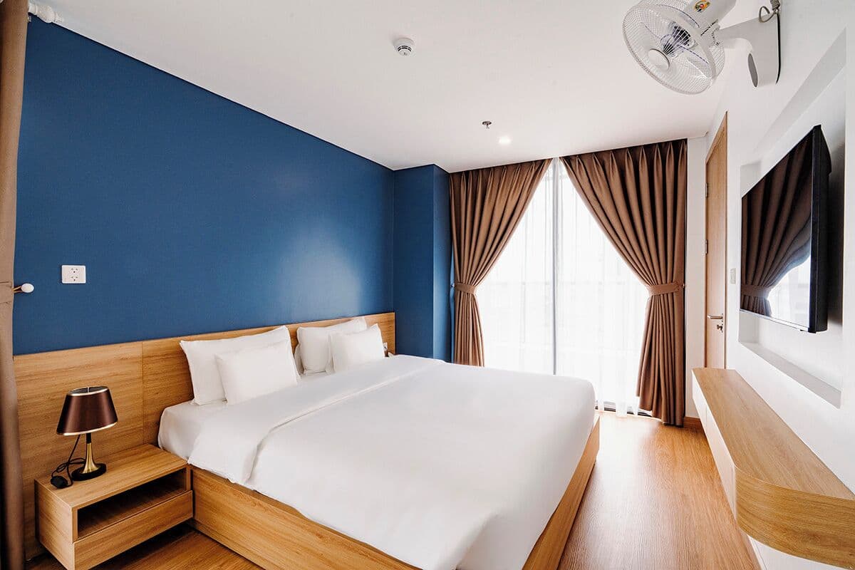 Een hotelkamer met een groot bed, een nachtkastje, een tv aan de muur en een plafondventilator.