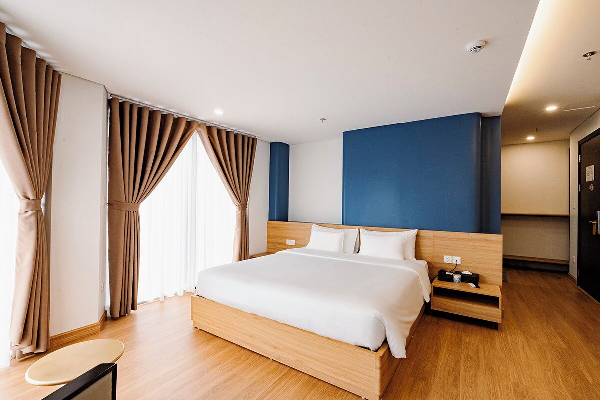 A modern hotel room with a wooden bed, a nightstand, a desk, and a wardrobe.