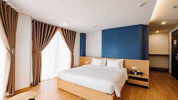 A modern hotel room with a wooden bed, a nightstand, a desk, and a wardrobe.