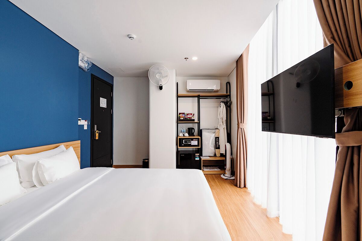 A hotel room with a bed, a TV, a wardrobe, and an air conditioning unit.