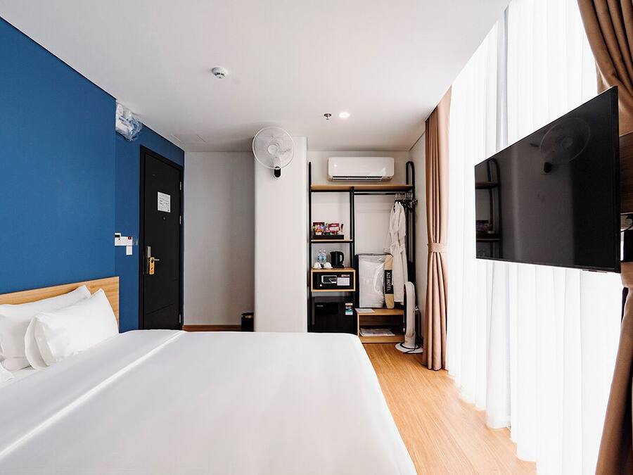 A hotel room with a bed, a TV, a wardrobe, and an air conditioning unit.