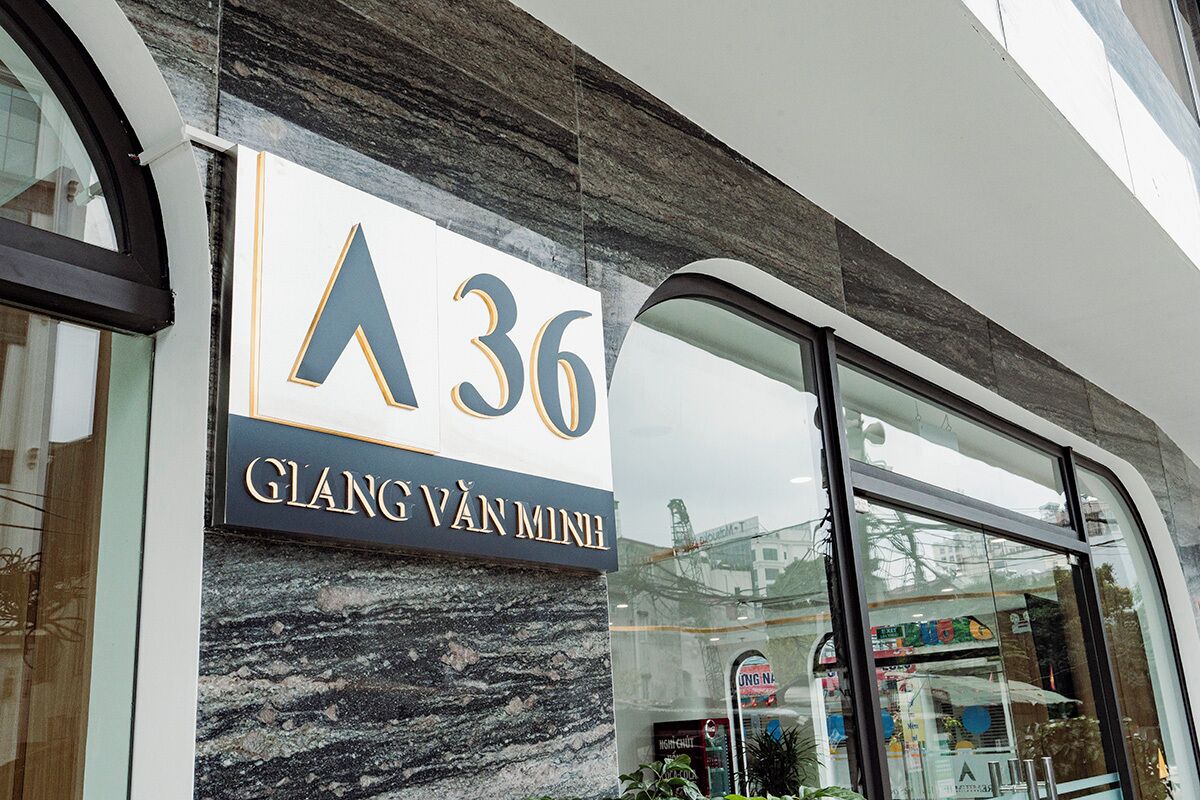 Un edificio con un letrero que dice 'A36 GLANG VĂN MINH' y el reflejo de una tienda con un letrero 'UNG NĂ'.