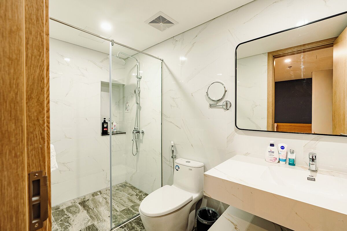 A modern bathroom with a glass shower enclosure, a toilet, a sink with toiletries, and a mirror.
