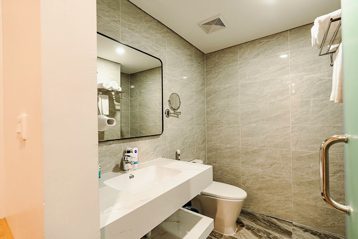 A modern bathroom with a marble wall, a white sink, a toilet, and a mirror.