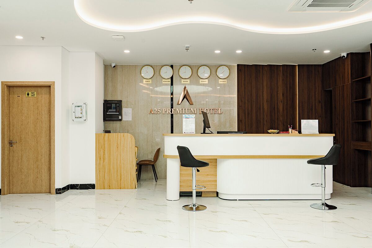 A reception area with a wooden reception desk, two bar stools, a clock, and a wall-mounted sign for A25 Premium Hotel.