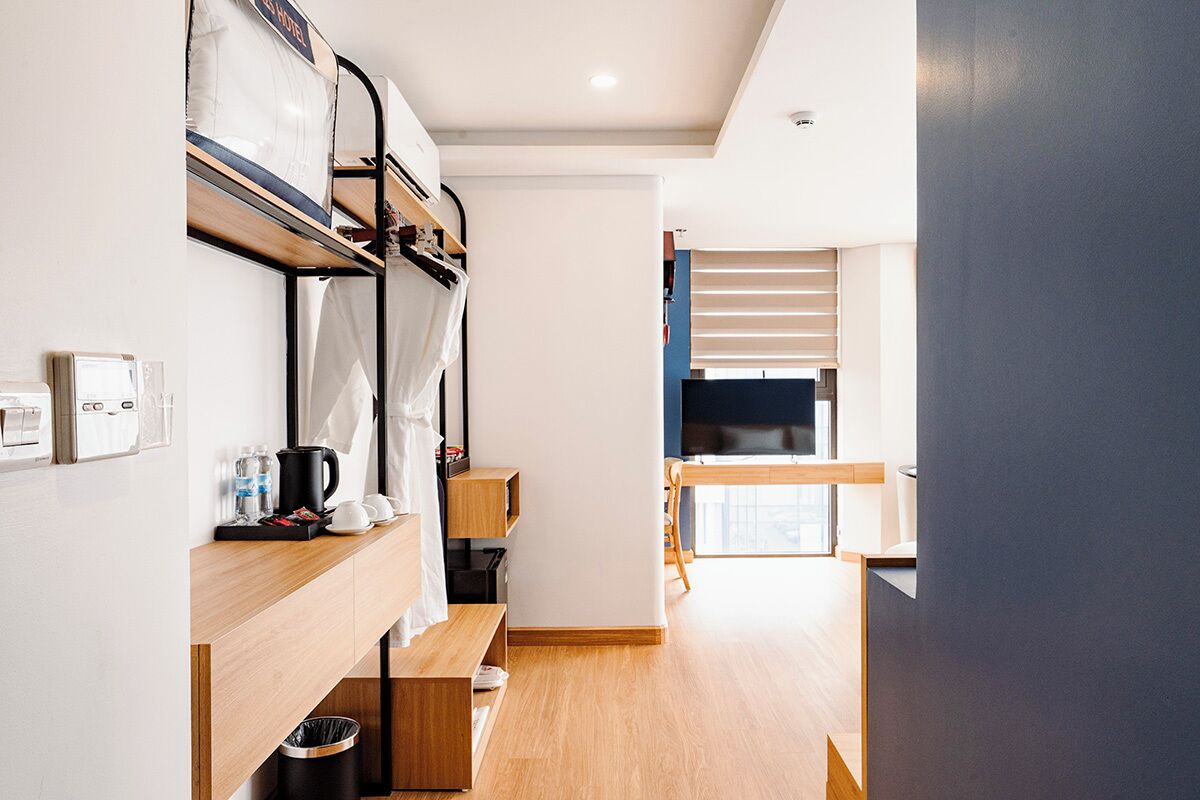 A modern hotel room with bunk beds, a kitchenette, a TV, and a large window.
