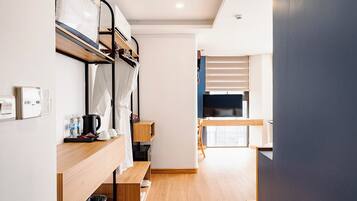 A modern hotel room with bunk beds, a kitchenette, a TV, and a large window.