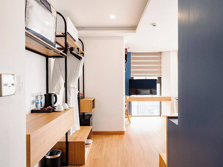 A modern hotel room with bunk beds, a kitchenette, a TV, and a large window.