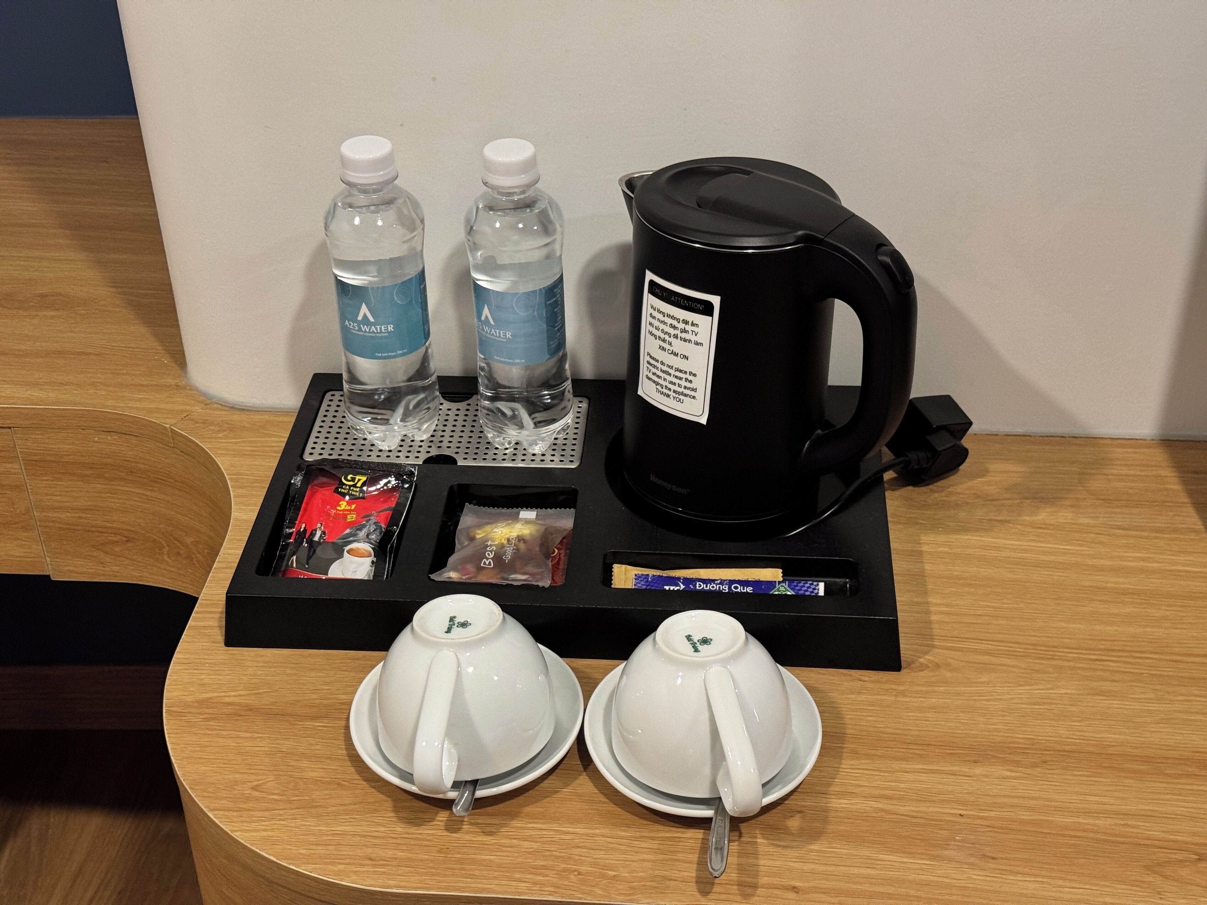 A hotel room's breakfast setup with a coffee maker, two water bottles, a tray with coffee and tea, and two teacups.