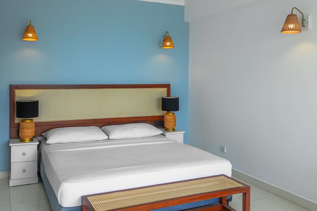 Una cama bien hecha con sábanas blancas, cabecera de madera y dos lámparas de noche.