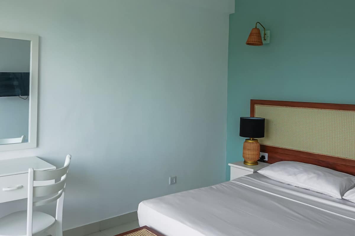 Un dormitorio con cama, mesita de noche con lámpara, una silla y un espejo en la pared.
