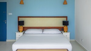 A bedroom with a large bed, two bedside tables with lamps, a wooden headboard, and a blue wall. - Mask & Tide - Jetwing Select (Ambalangoda)
