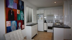 A compact kitchen with white cabinets, a black countertop, and a white chair. - Belong At Bendalong is a large family home (Bendalong)