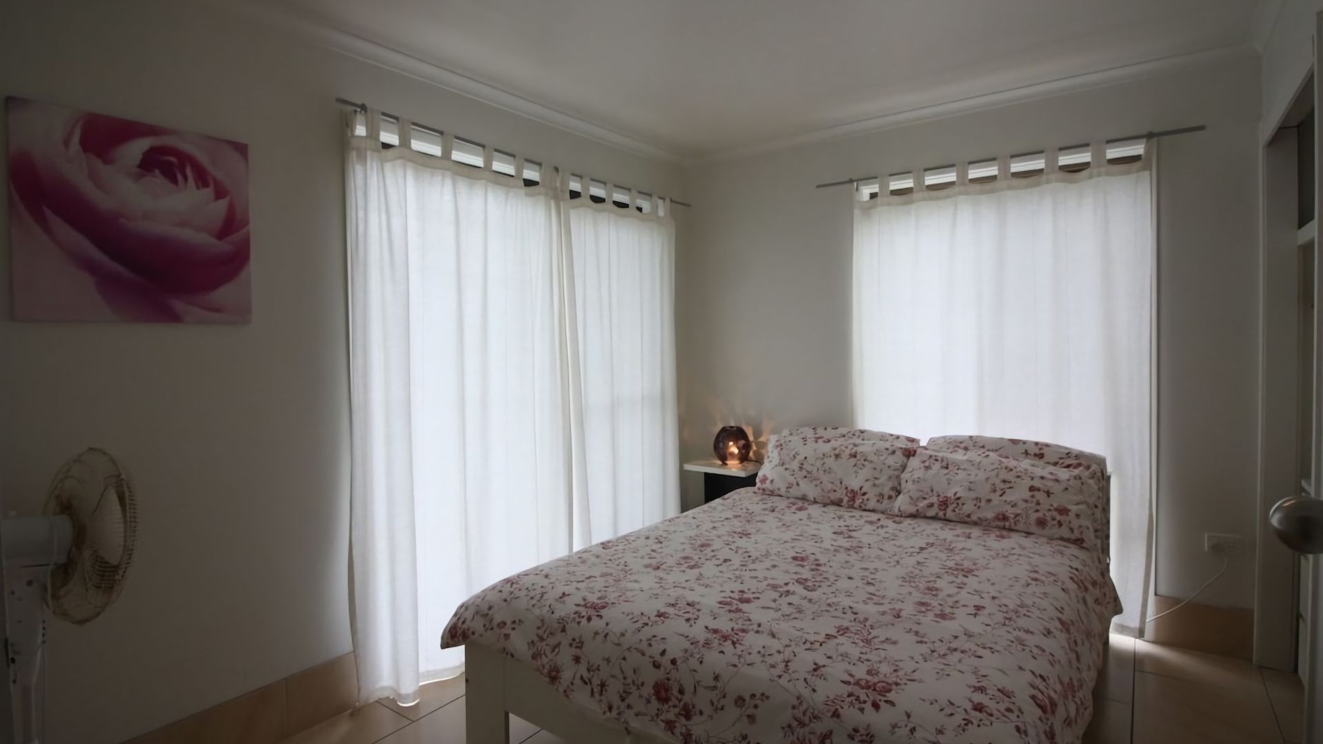Une chambre à coucher avec un lit, une table de chevet avec une lampe et un ventilateur fixé au mur.