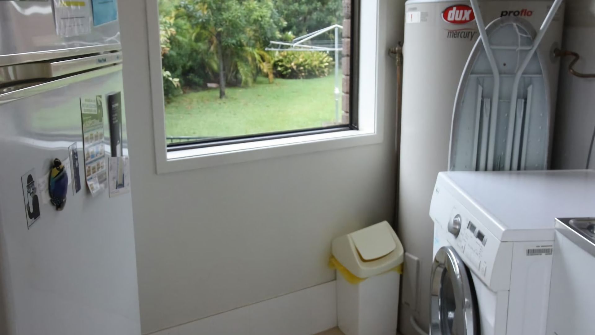A laundry room with a washing machine, a dryer, and a window with a view of a garden.