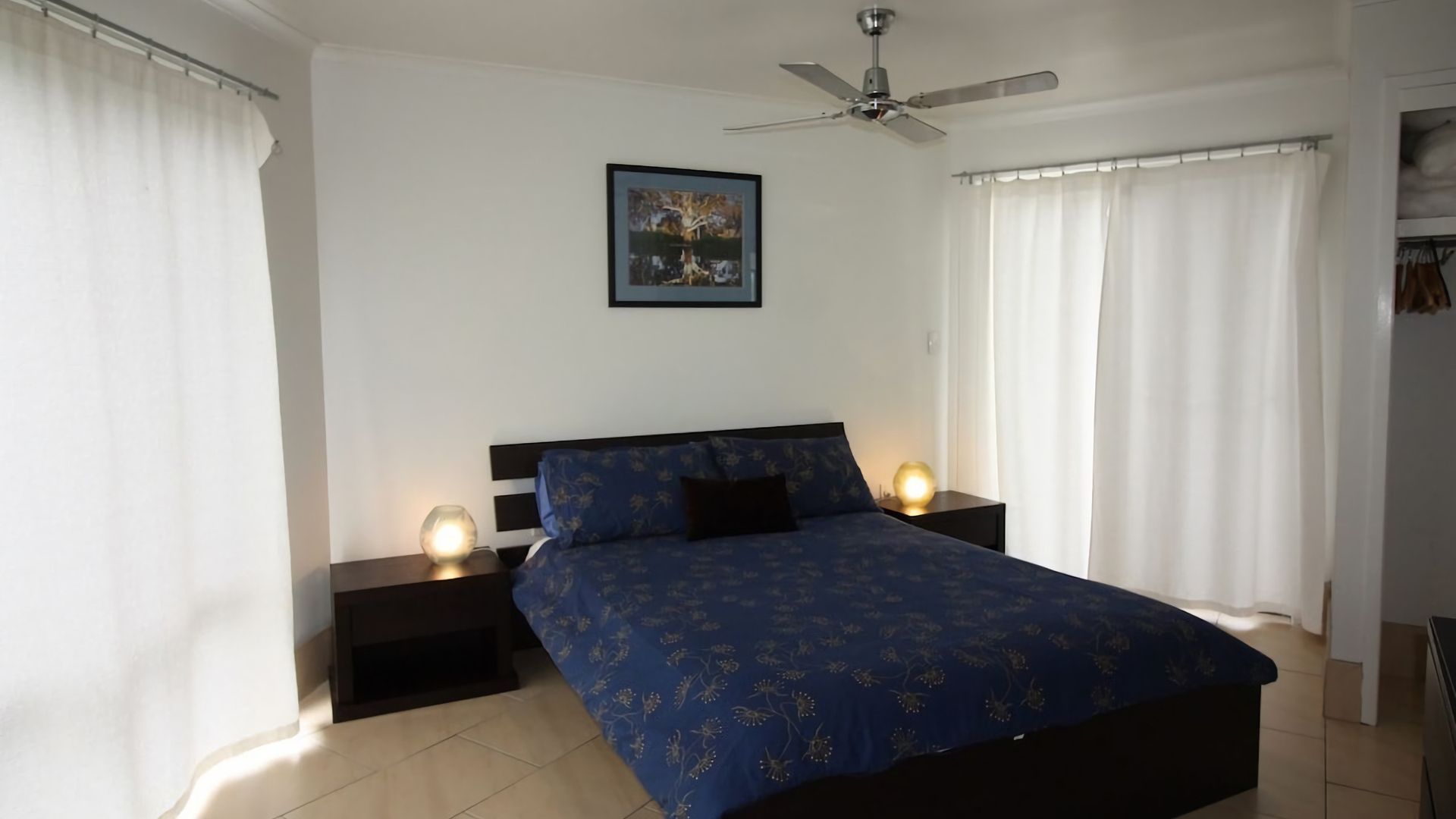 Ein Schlafzimmer mit einem Bett, zwei Nachttischen, einem Deckenventilator und einem Gemälde an der Wand.