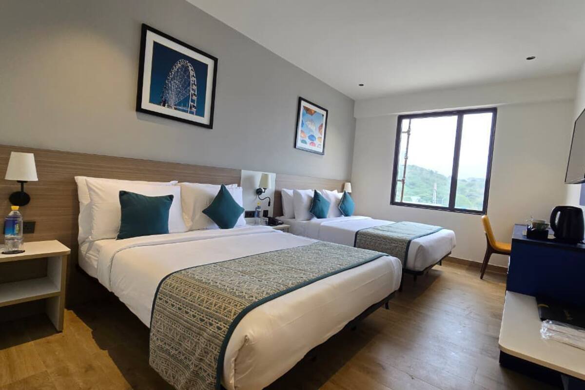 Camera d'albergo con due letti, una scrivania, una sedia, una TV e una finestra con vista.