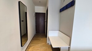 Un pasillo estrecho con piso de madera, un banco blanco y un espejo grande en la pared izquierda.