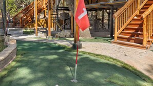A miniature golf course with a red flag, wooden stairs, and a green artificial turf. - San Antonio Area Treehouse – Hill Country Hi View Landing (Lakehills)