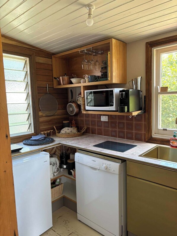 A compact kitchen with wooden cabinets, a microwave, a coffee maker, and a dishwasher.