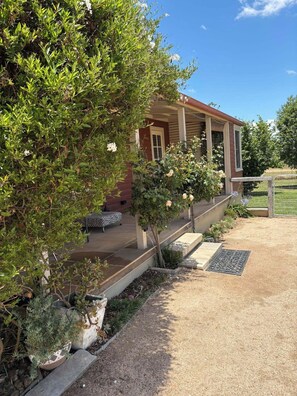 Une maison avec un porche abrité, un jardin où poussent différentes plantes et un ciel bleu dégagé.
