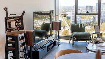 A modern room with a large window, a vintage film camera, a green armchair, and a table with a lamp.