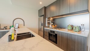 Uma cozinha moderna com bancada de mármore, armários de madeira, forno embutido e geladeira de aço inoxidável.