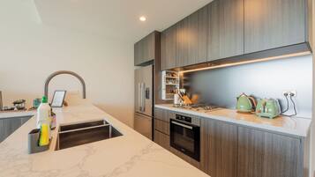 A modern kitchen with a marble countertop, wooden cabinets, a built-in oven, and a stainless steel refrigerator.