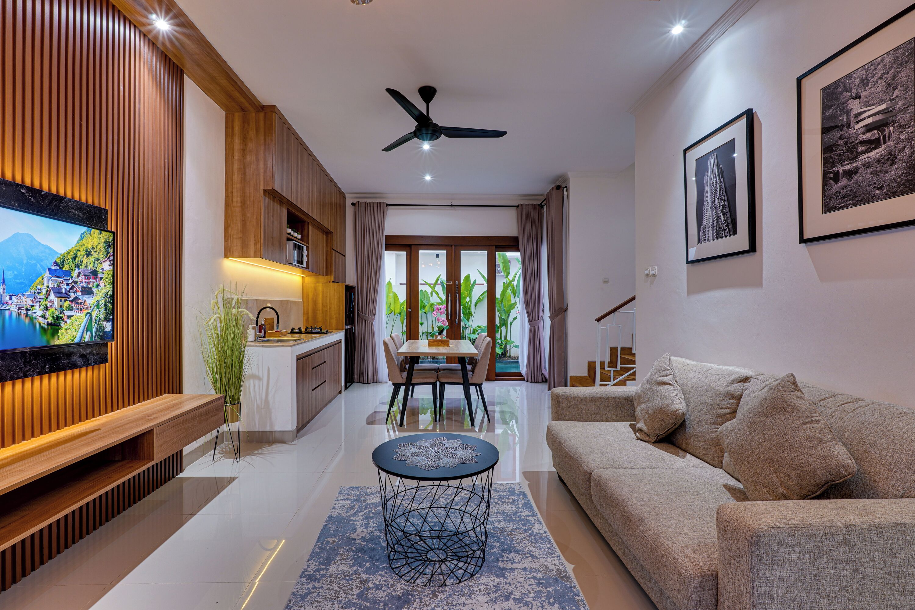 A modern living room with a sofa, a coffee table, a TV, wooden paneling, a ceiling fan, and a dining area with a table and chairs.