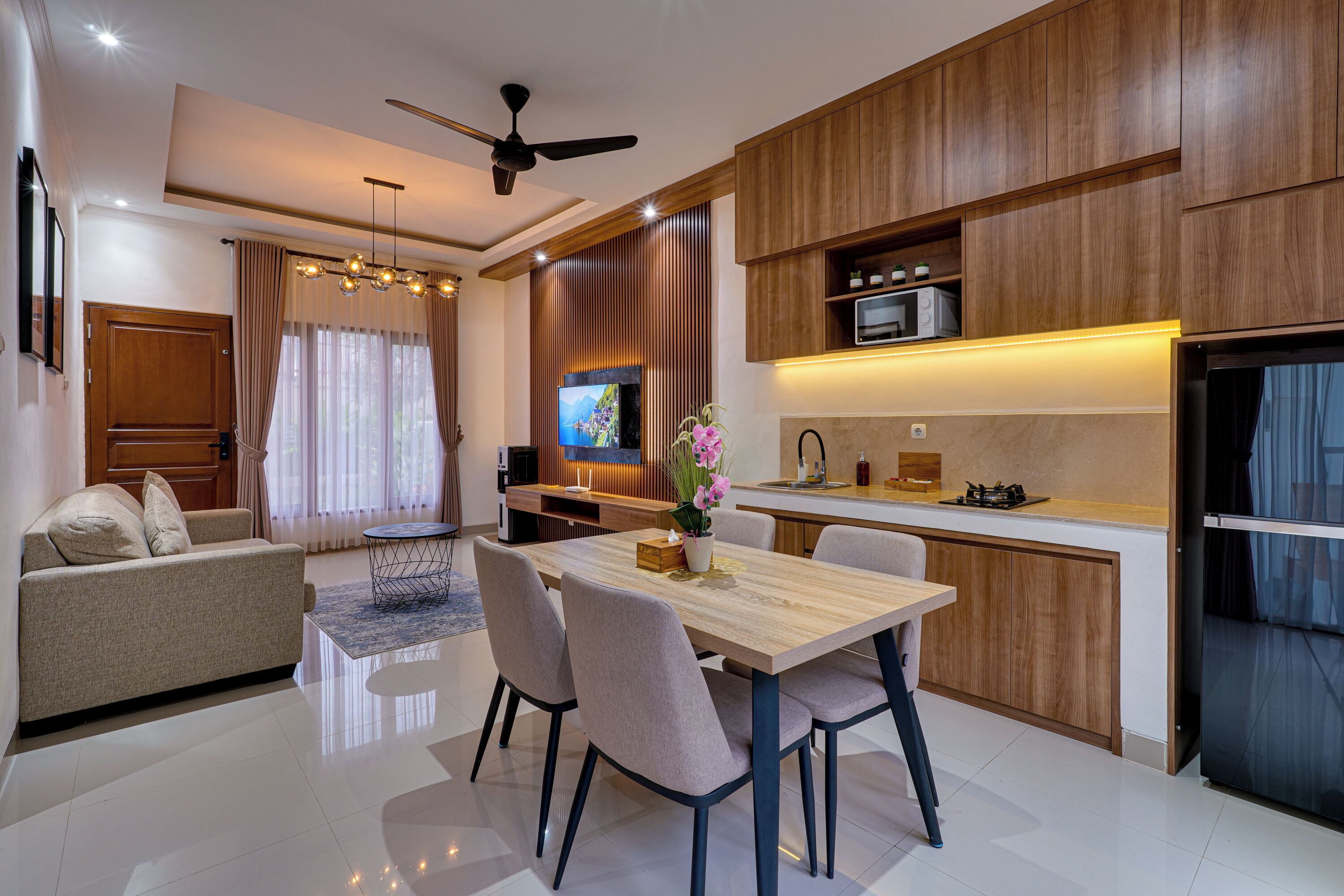 A modern kitchen with wooden cabinets, a dining area with a table and chairs, and a living room with a sofa and curtains.