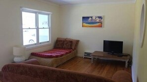 A living room with a sofa, a television on a stand, a window, and a painting on the wall. - Driftwood in the heart of Bendalong (Bendalong)