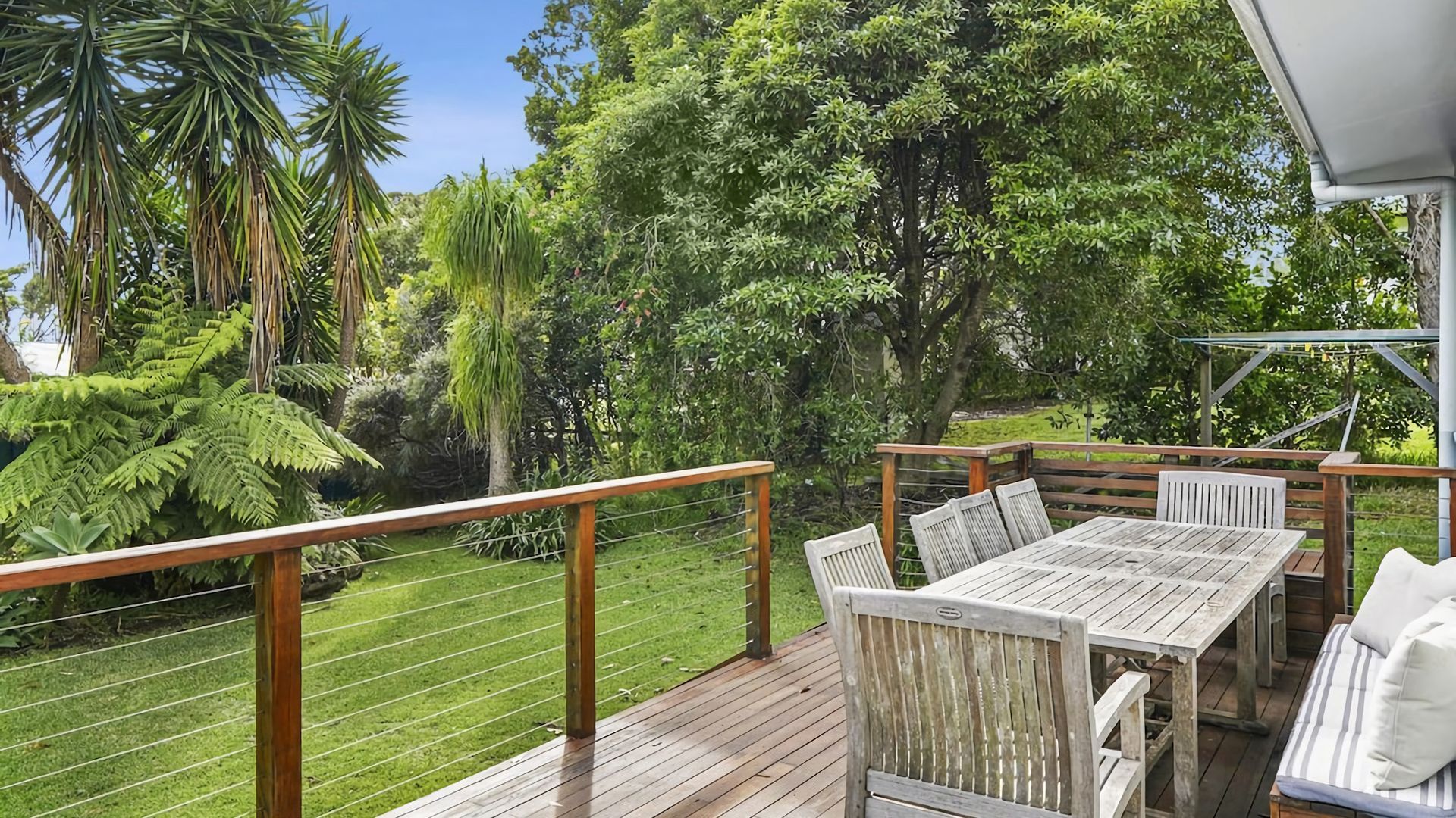 A deck with a wooden table and chairs, surrounded by lush greenery and trees.