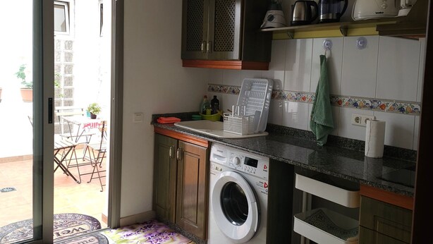 A compact kitchen with a washing machine, a coffee maker, and a clock on the wall. - Charming Holiday House in Las Palmas with City Views (Telde)