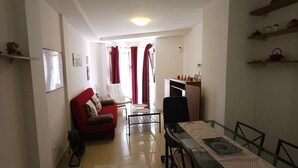 A spacious living area with a red sofa, a dining table with chairs, and a kitchen area in the background. - Charming Holiday House in Las Palmas with City Views (Telde)