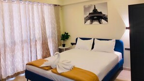 Una habitación de hotel con una cama, ventilador de techo, aire acondicionado, planta en maceta y un cuadro de la Torre Eiffel.