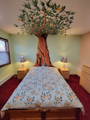 A bedroom with a bed, two bedside tables, a dresser, and a wall-mounted tree decoration.