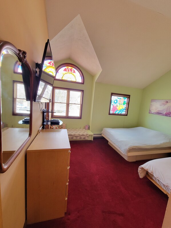Quarto com escrivaninha, duas camas, espelho e duas janelas com vitrais.