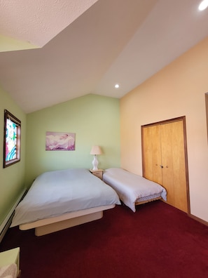 A bedroom with a bed, a nightstand, a lamp, a wooden wardrobe, and a painting on the wall.