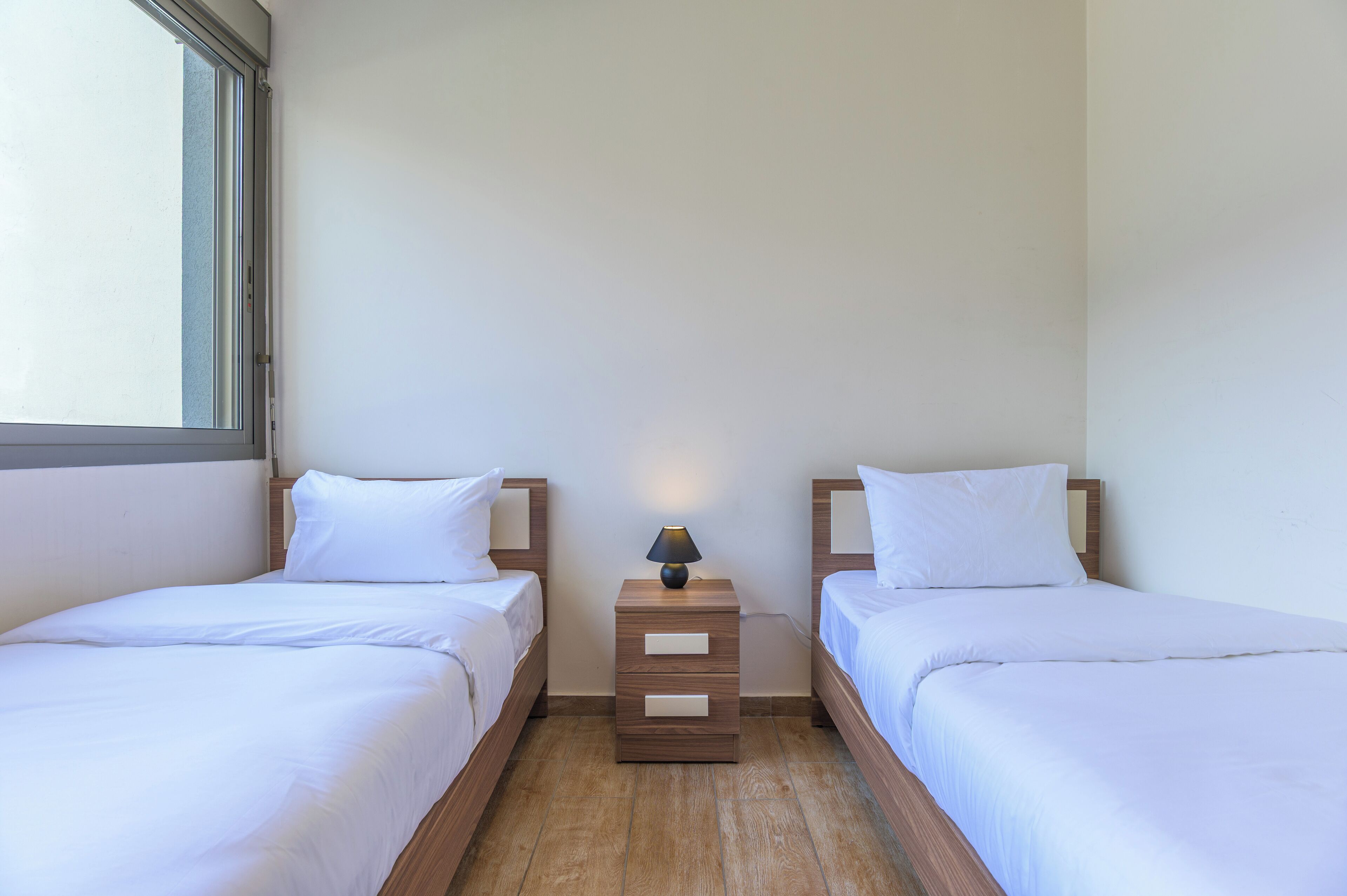 A twin room with two beds, a nightstand with a lamp, and a window.