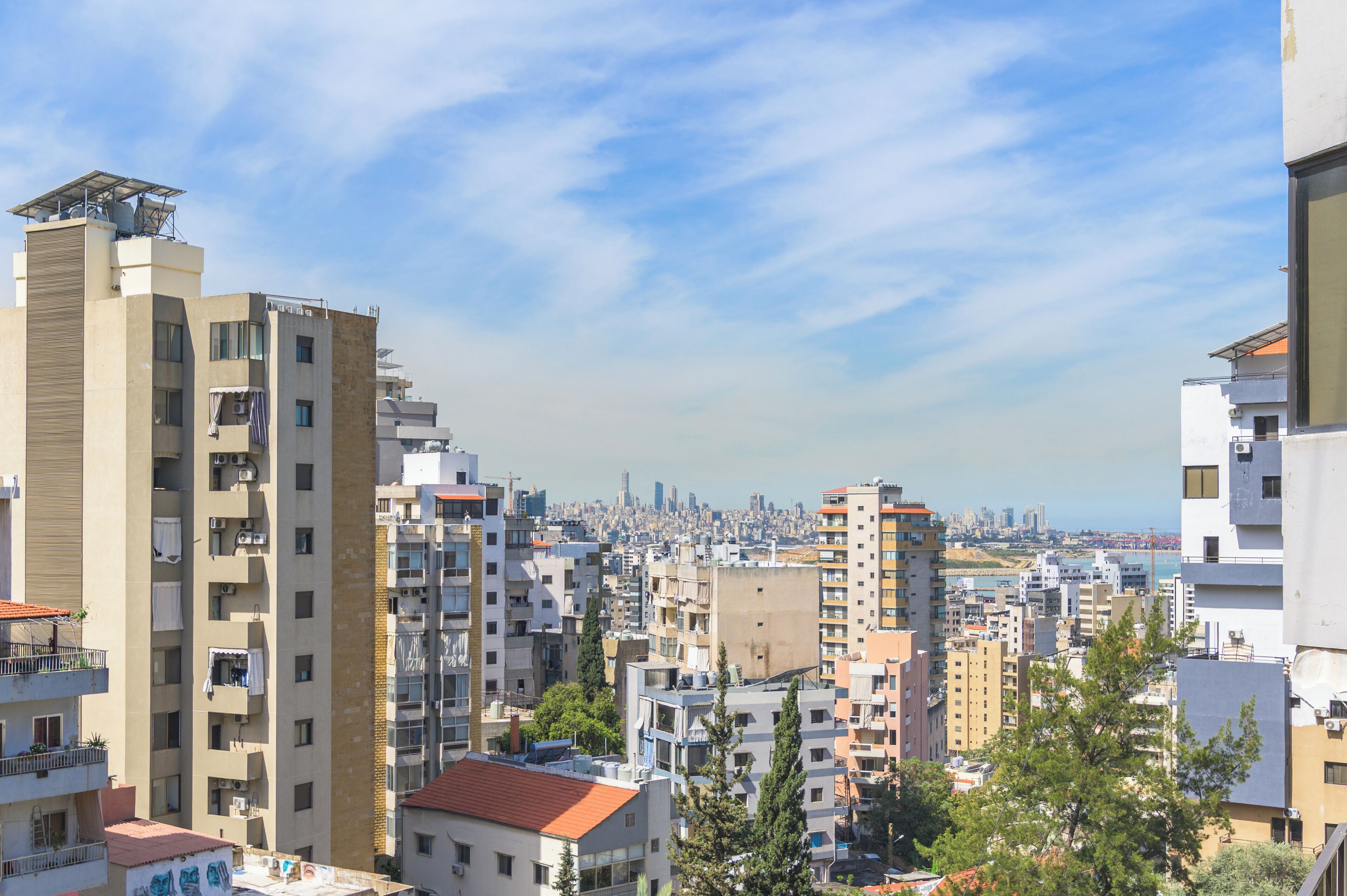 Um edifício residencial alto com várias varandas, um horizonte urbano ao fundo e céu claro.