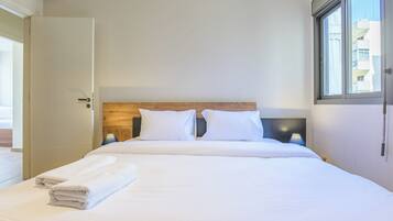 Une chambre d’hôtel avec un lit, deux oreillers, une tête de lit en bois, une fenêtre et une porte.