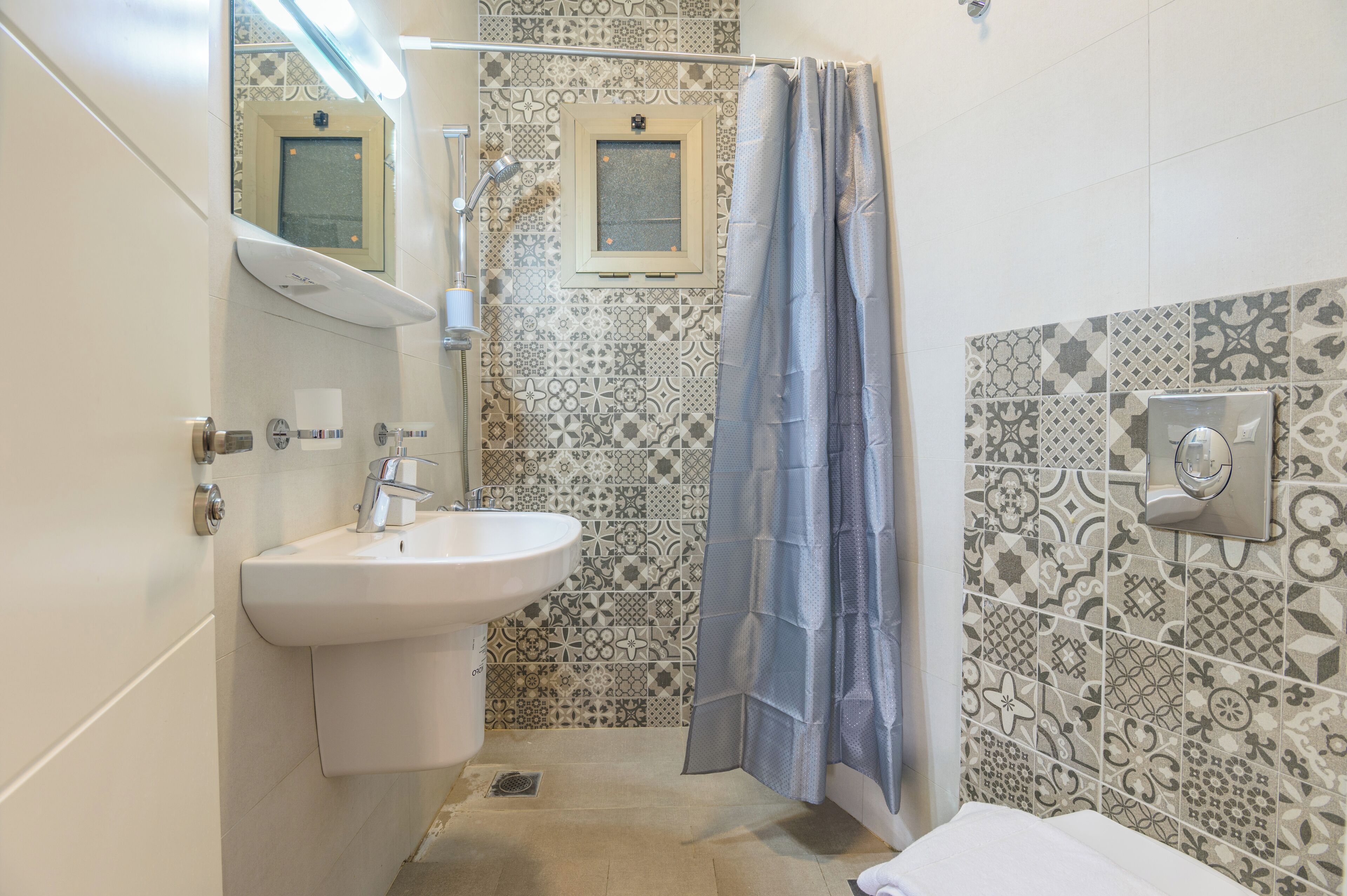 Un baño con lavamanos, espejo, cortina de ducha y azulejos estampados.