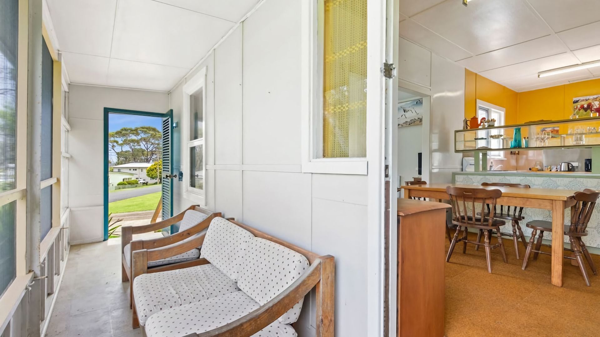 A room with a wooden bench, a dining table with chairs, and a kitchen area with a counter and various items.