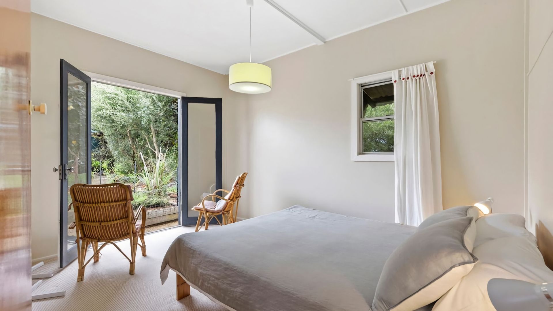 A bedroom with a bed, two chairs, a window with curtains, and a door leading to an outdoor area.
