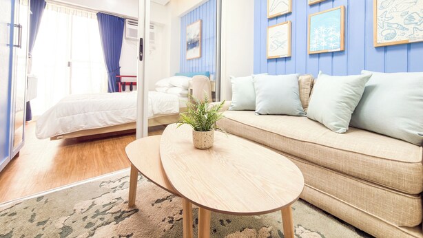 A modern hotel room with a bed, a sofa, a small table, and a potted plant. - Verdon Parc Davao City Condo - Perfect Staycation Near SM Ecoland (Davao City)