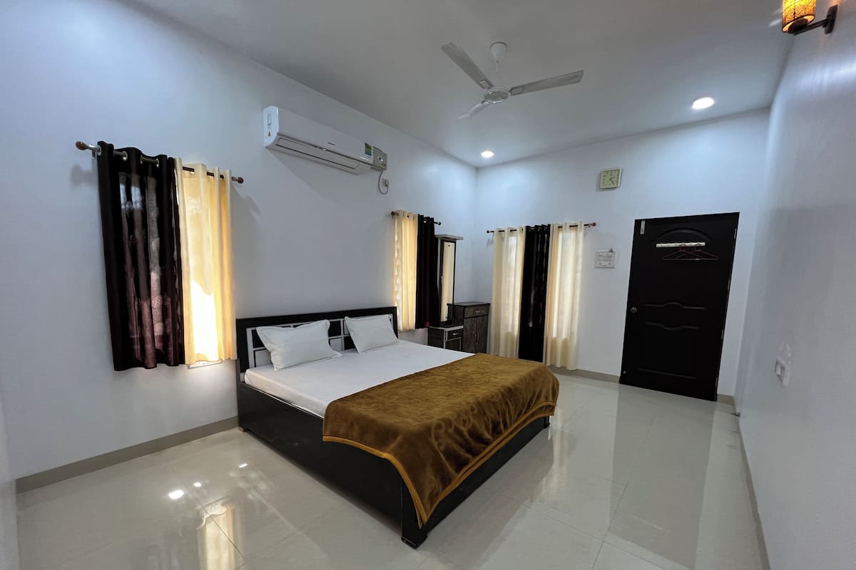A hotel room with a bed, a ceiling fan, an air conditioning unit, a wardrobe, and a door.