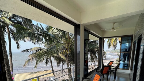 Un balcone con vista sulla spiaggia e palme, arredato con sedie e tavoli.