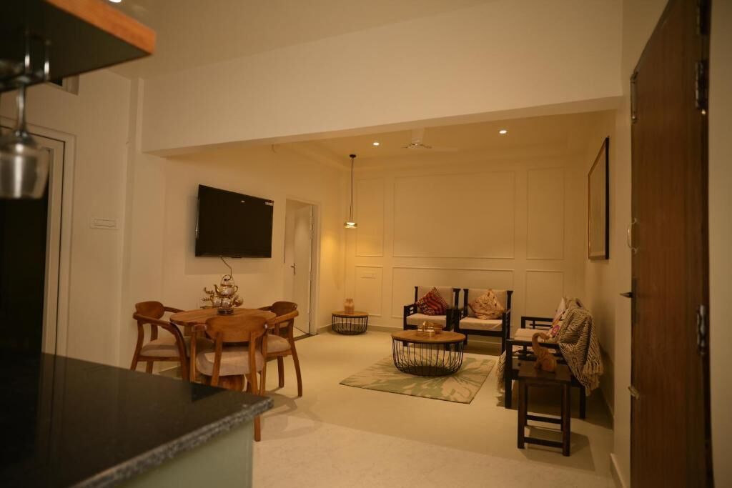 A living room with a sofa, coffee table, and chairs, a dining area with a table and chairs, and a TV mounted on the wall.