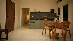 A compact kitchen with a dining area, featuring a wooden table and chairs, a green cabinet, and a tiled backsplash. - Noi Homes (East Jorhat)