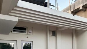 A modern building with a flat roof, white exterior walls, and a visible air conditioning unit. - Noi Homes (East Jorhat)